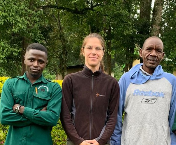 Three people, two black men and one white woman, stand in front of trees