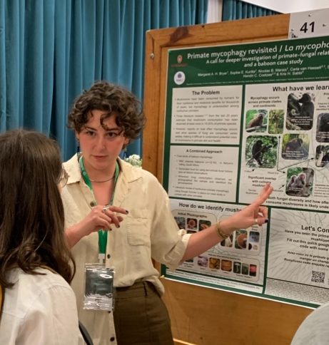 White woman with brown curly hair talks to second person about scientific poster