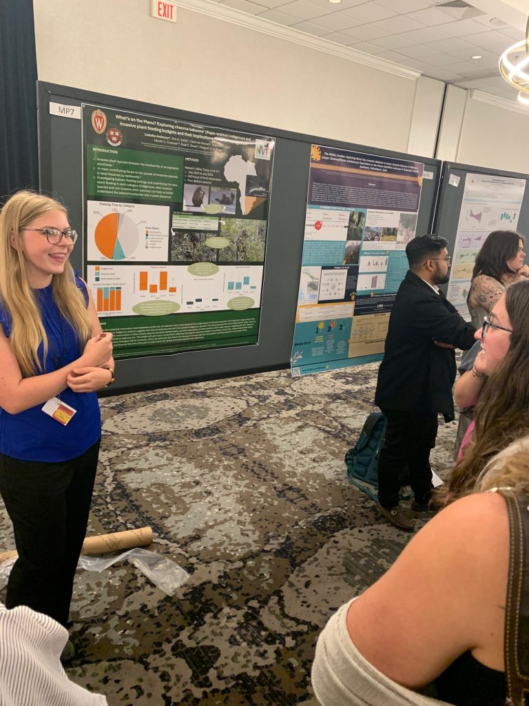 A white woman with blonde hair presents her scientific poster to other students