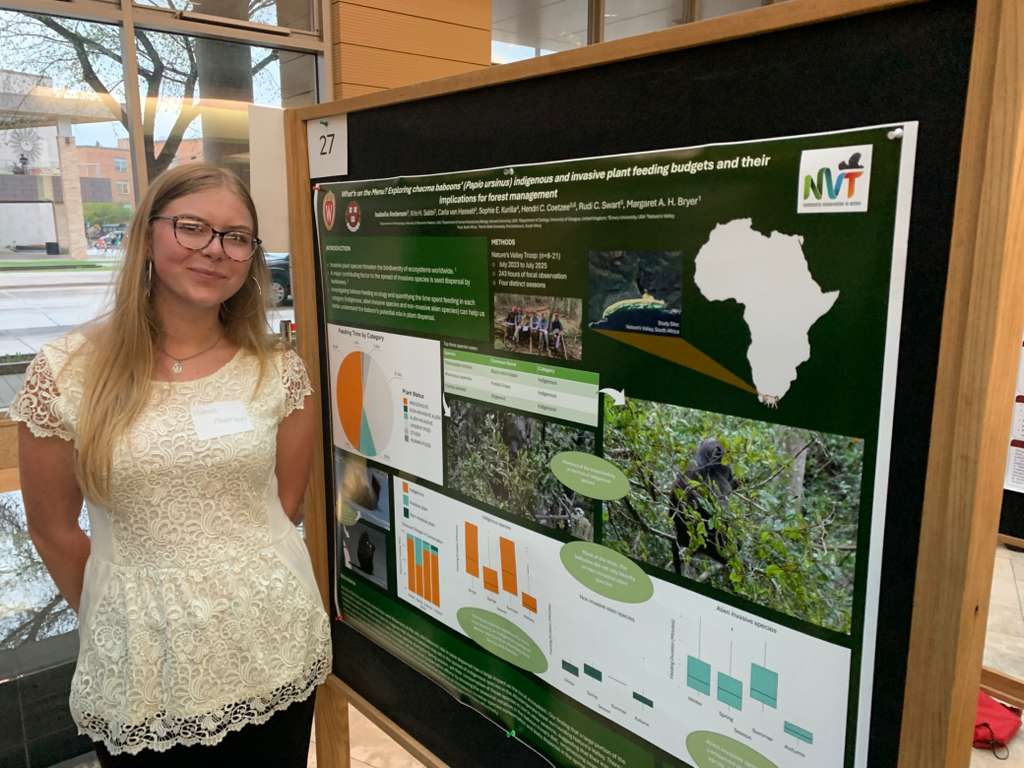 White woman with blonde hair stands in front of a scientific poster
