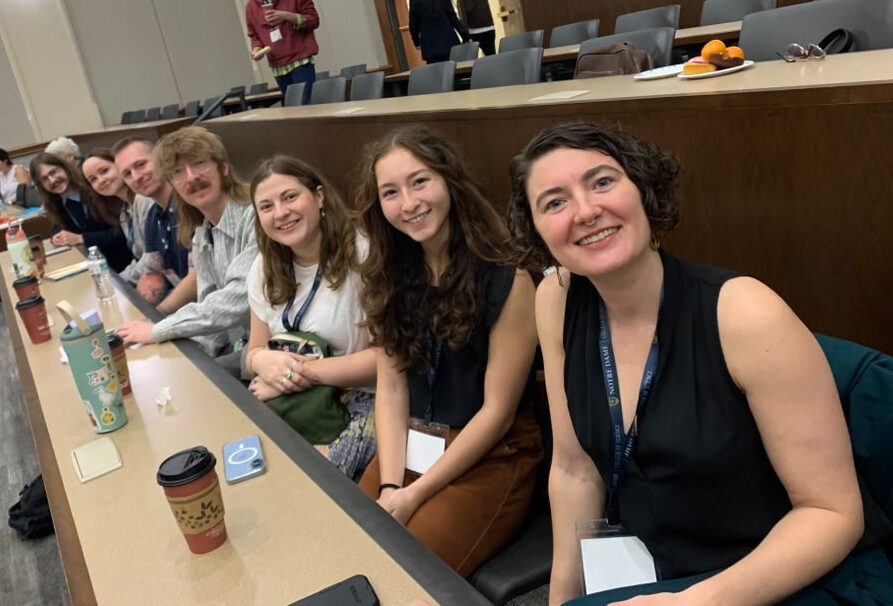 Seven people sitting in a row at a conference smiling